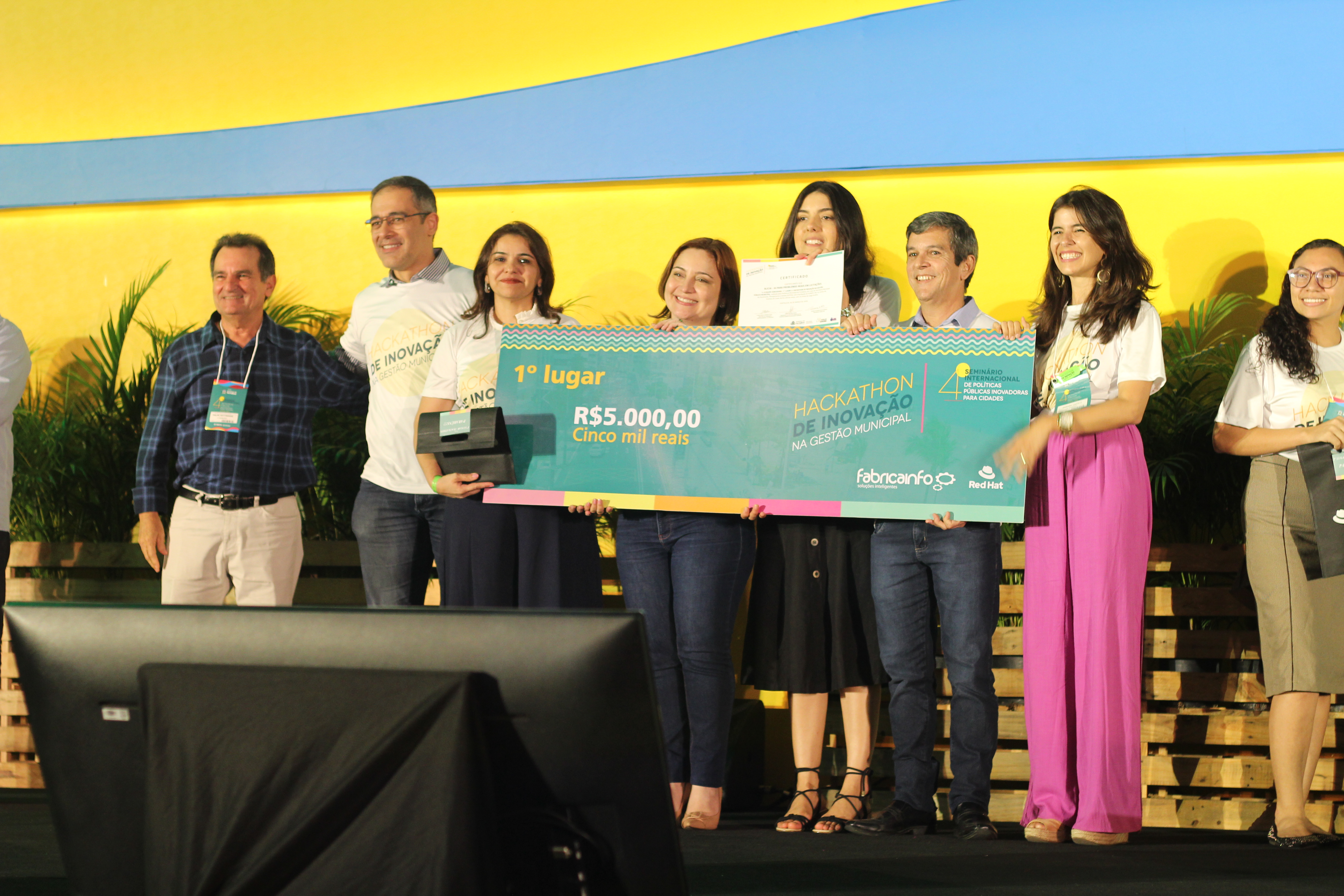 oito pessoas em cima de palco sorrindo e segurança cheque gigante